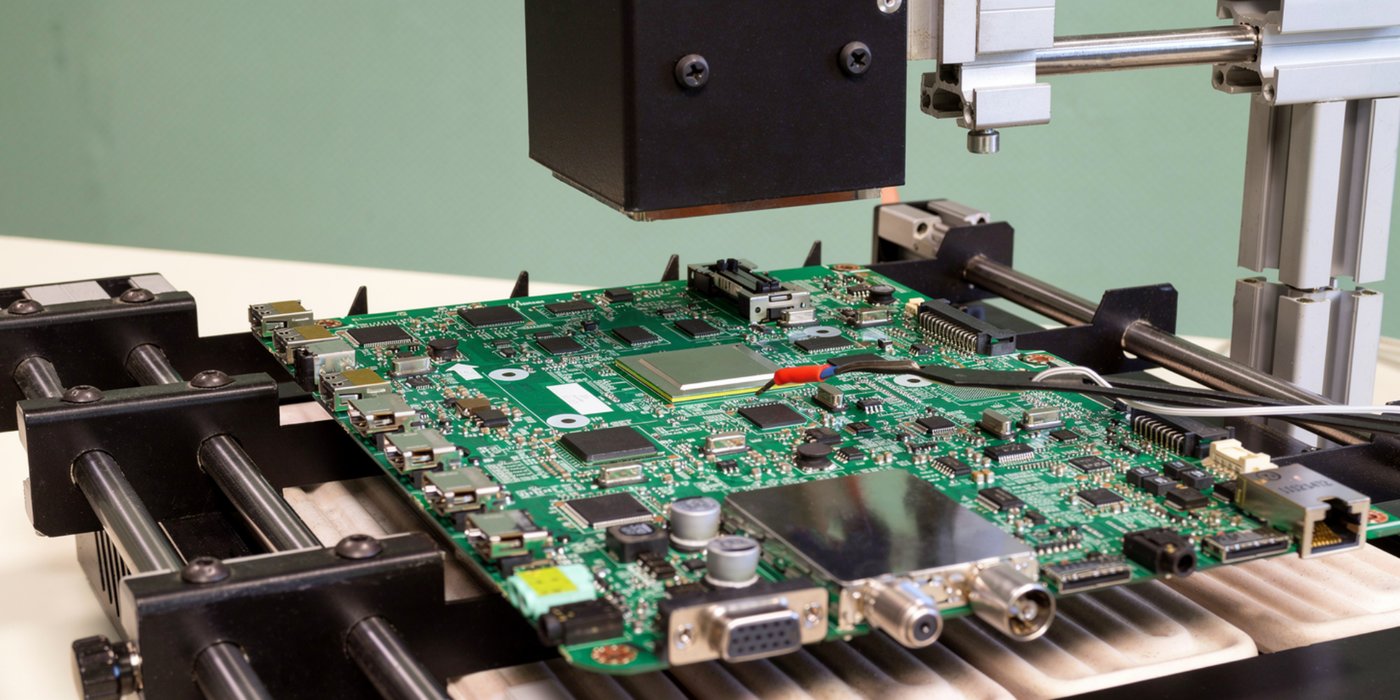 Populated motherboard mounted in an automated BGA rework station with overhead heating head